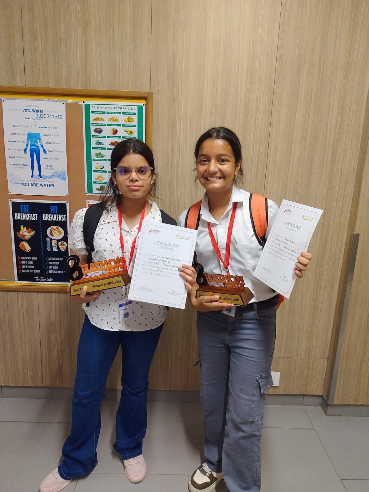 Two students holding competition trophies and certificates